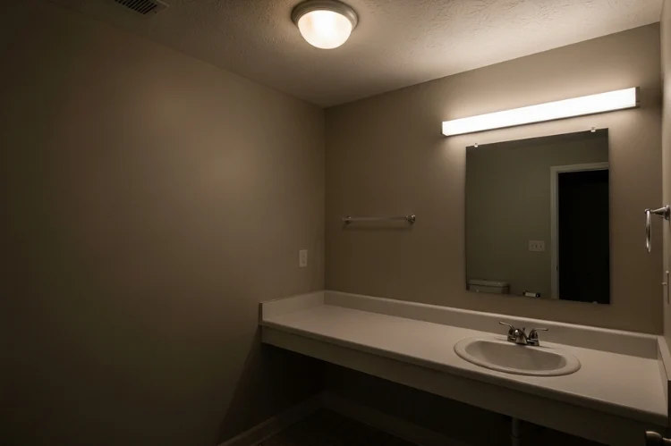 Basic frosted dome flush mount ceiling light in small bathroom, dim uneven vanity lighting, generic new construction home style, flat uninspiring atmosphere
