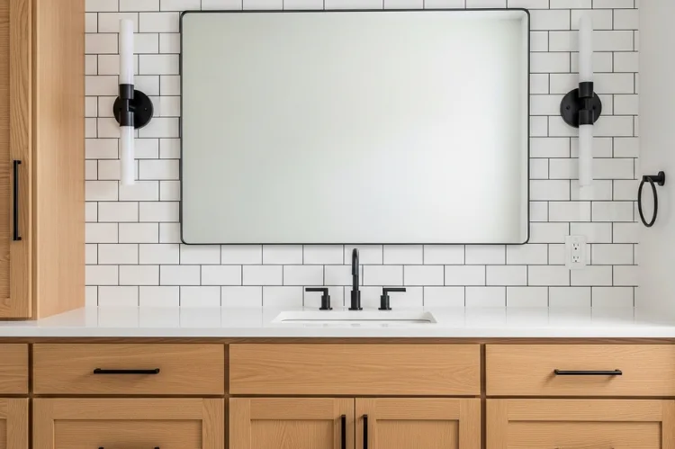 Bathroom vanity with matte black wall sconces beside mirror, matching matte black faucet and cabinet handles, white subway tile backsplash