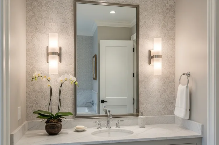 Two wall sconces mounted beside bathroom mirror at eye level, balanced cross-lighting