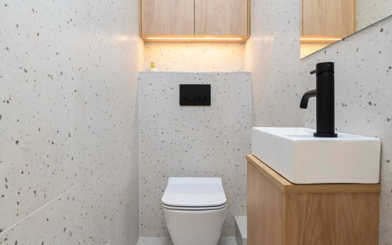 Small bathroom ideas featuring a modern terrazzo tile design with a wall-mounted toilet and compact wooden vanity.