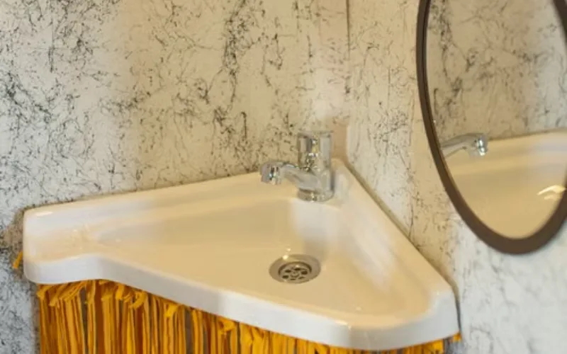 ompact white corner sink with yellow fringe trim.